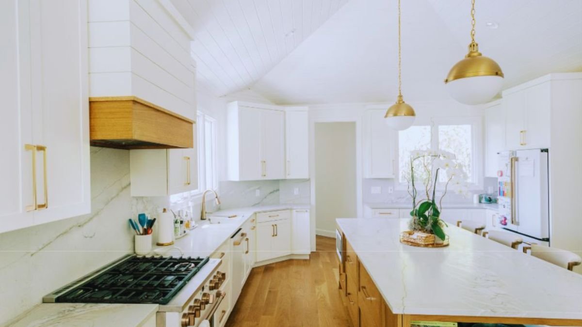 Bright custom home kitchen with white cabinetry, marble countertops, wood accents, pendant lighting, a large island, and modern appliances in an open-concept design.