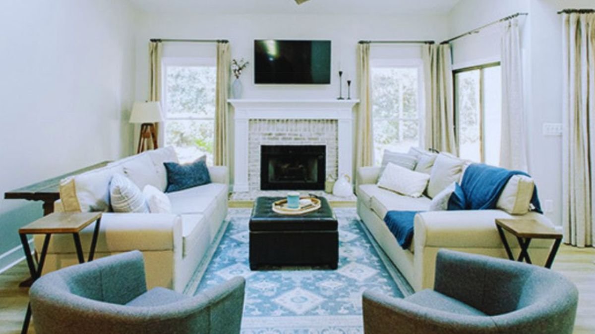 Bright custom-built living room featuring modern white sofas, gray accent chairs, a fireplace with mounted TV, large windows with natural light, and stylish contemporary décor.